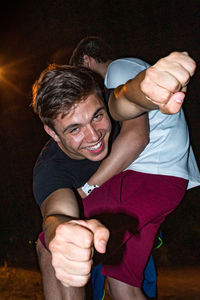 Portrait of smiling man clenching fist being carried by friend at night