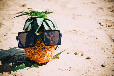 High angle view of sunglasses with pineapple on sand at beach