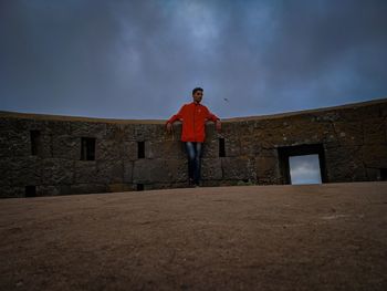 Low angle view of man standing by building against sky