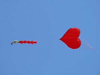 Low angle view of kites flying against clear blue sky