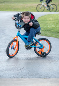 Cute little boy shows off as he learns to ride his first bike with training wheels