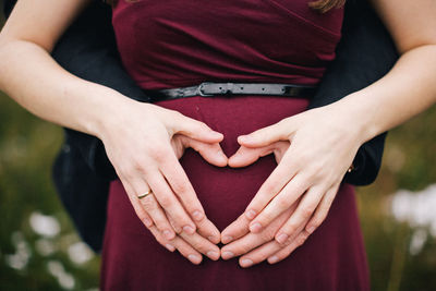 Midsection of couple making heart shape on pregnant belly