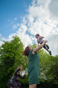 Low angle view of mother tossing daughter in air against tree
