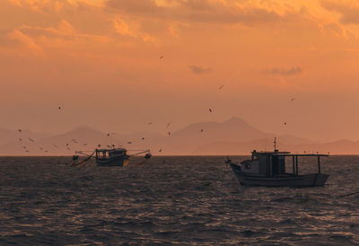 Fishing boats in sea at sunset