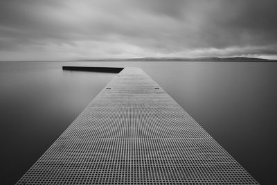 Pier on lake against cloudy sky