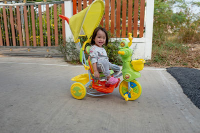 Portrait of smiling girl riding tricycle on footpath