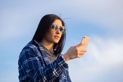 Portrait of young woman using mobile phone against sky