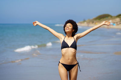 Happy young woman with arms outstretched enjoying sunlight at beach