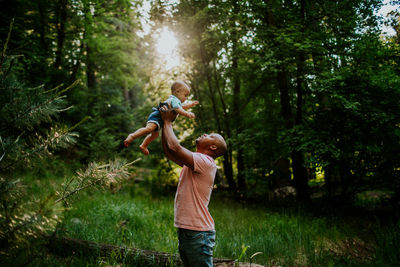 Dad holding infant son up in the air in the middle of forest