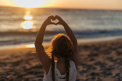 Girl making heart with her hand on the beach on sunset