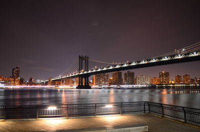 Illuminated bridge over river with city in background at night