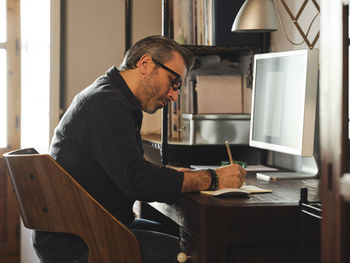 Man working at home desk with computer via internet taking notes