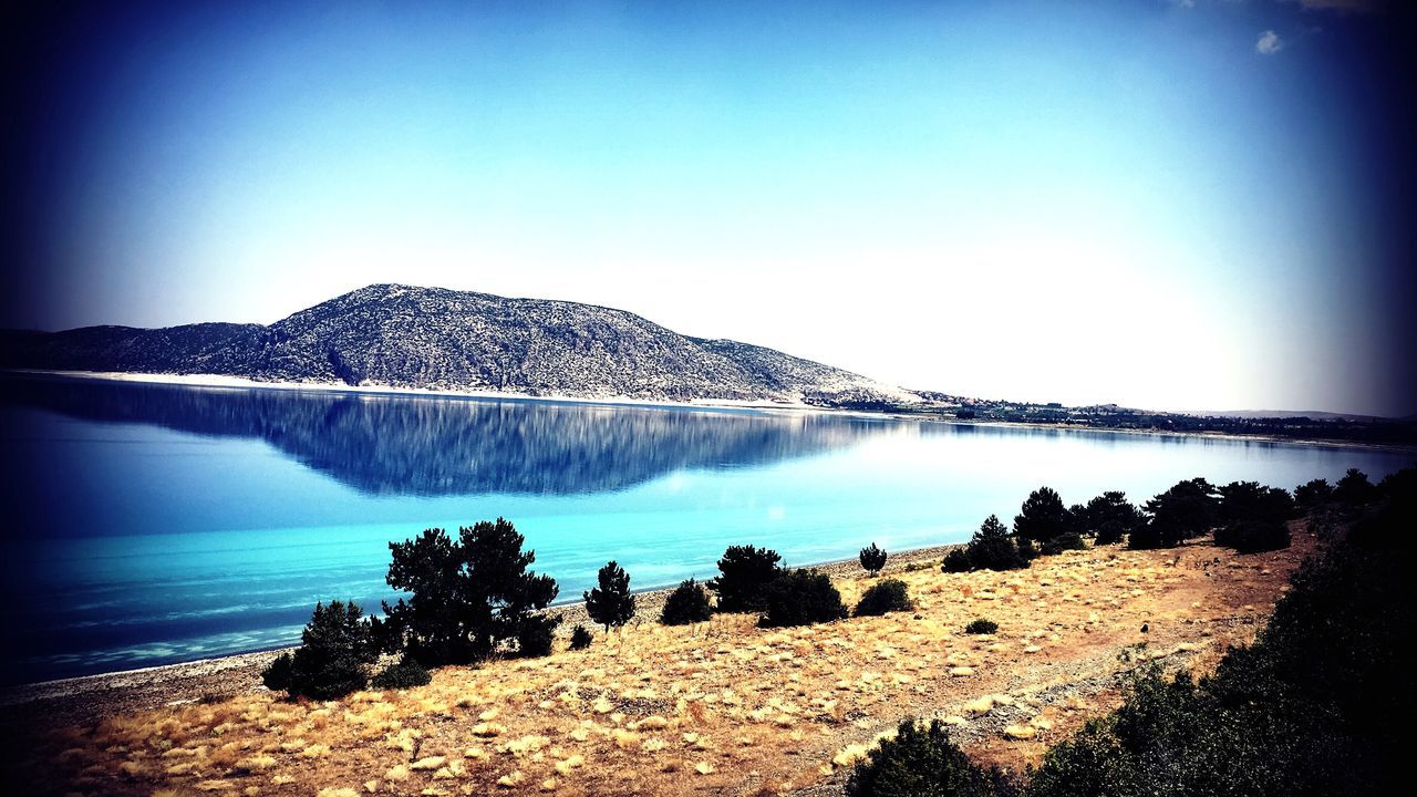 water, tranquil scene, vignette, scenics, clear sky, tranquility, blue, tourism, majestic, beauty in nature, travel destinations, geology, non-urban scene, calm, reflection, vacations, nature, physical geography, sea, mountain, rock formation, day, summer, sky, ethereal