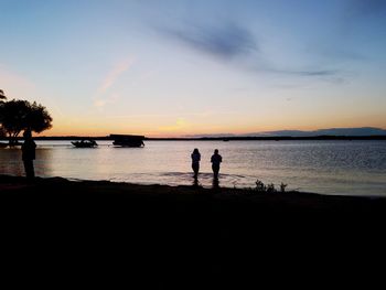 Silhouette people on beach against sky during sunset