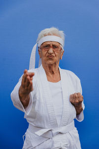 Portrait of senior woman doing karate against blue background