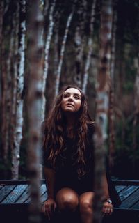 Young woman looking away while sitting on tree in forest