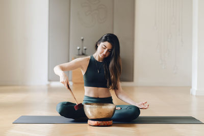 Woman playing rin gong while sitting on exercise mat 