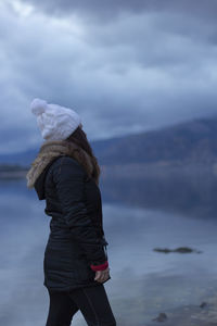 Woman looking away while standing by lake against sky