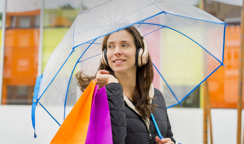 Smiling woman holding umbrella and shopping bags
