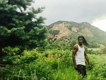 Portrait of man with dreadlocks standing on field against sky