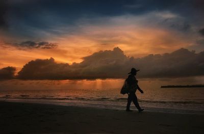 Silhouette man walking on beach against sky during sunset