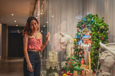 Portrait of smiling young woman standing against illuminated christmas tree