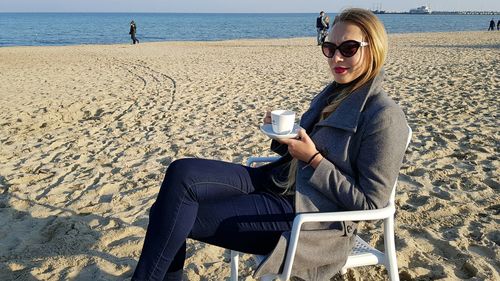 Woman having coffee while sitting at beach