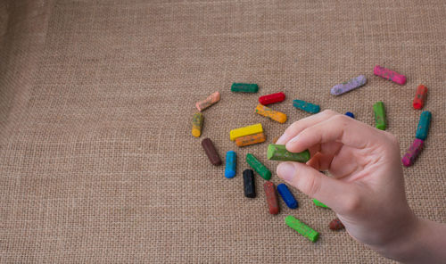Cropped hand of child making heart shape with colorful crayons on table
