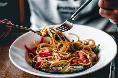 Close-up of hand holding noodles in plate