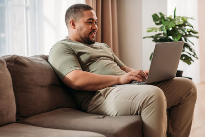 Smiling man using laptop while sitting on sofa at home