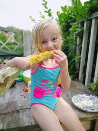 Portrait of cute girl eating corn while sitting on floorboard outdoors