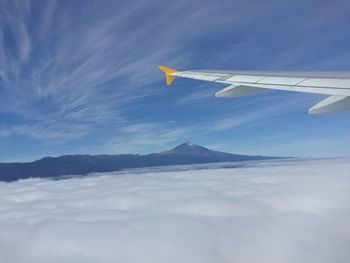 Cropped image of airplane over clouds against sky on sunny day