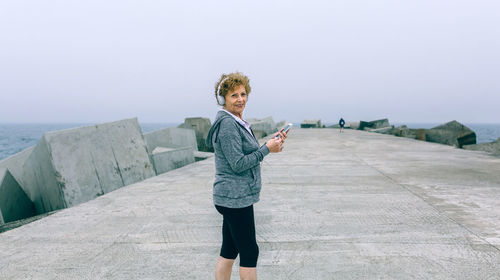 Senior woman standing on pier at beach against sky
