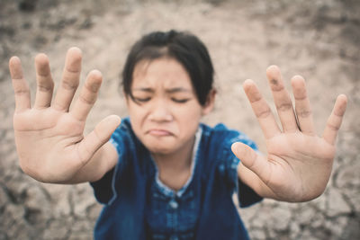 High angle view of girl showing hands on cracked field