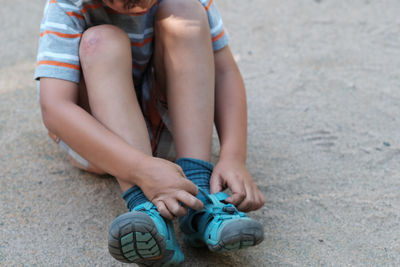 Low section of boy wearing shoes while sitting on sand