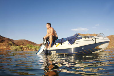 Man looking away while sitting in motorboat against sky