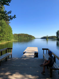 Woman sitting on pier by lake against clear sky