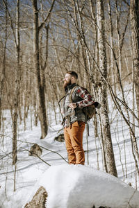 Man with beard wearing flannel stands on snow covered rock