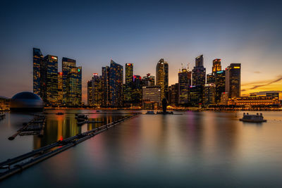 Illuminated buildings by river against sky in city