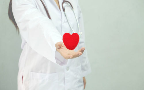 Close-up of female doctor holding heart shape against gray background