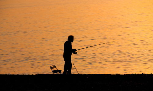 Silhouette man fishing in sea against sunset sky