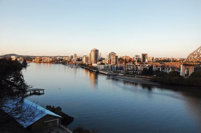 Buildings by river against clear sky in city