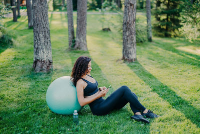 Woman with smart phone sitting by fitness ball in park