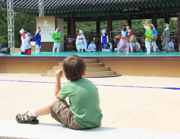 Rear view of boy looking at dance performance while sitting in city