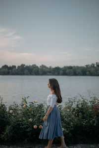 Young woman standing by plants against sky