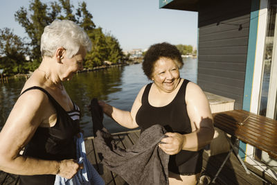 Happy senior female friends holding towel while standing on houseboat at sunny day