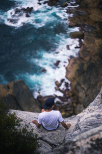 High angle view of man sitting on rock edge over sea