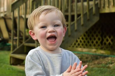 Portrait of laughing baby boy standing at yard