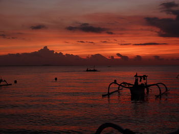 Silhouette outrigger boat moored in sea against sky during sunset