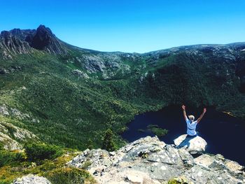 Woman with arms raised sitting on rock against lake